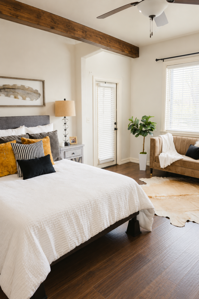 Cozy bedroom decor with white bedding, mustard yellow accent pillows, a gray upholstered headboard, and a beige loveseat with a soft throw blanket.