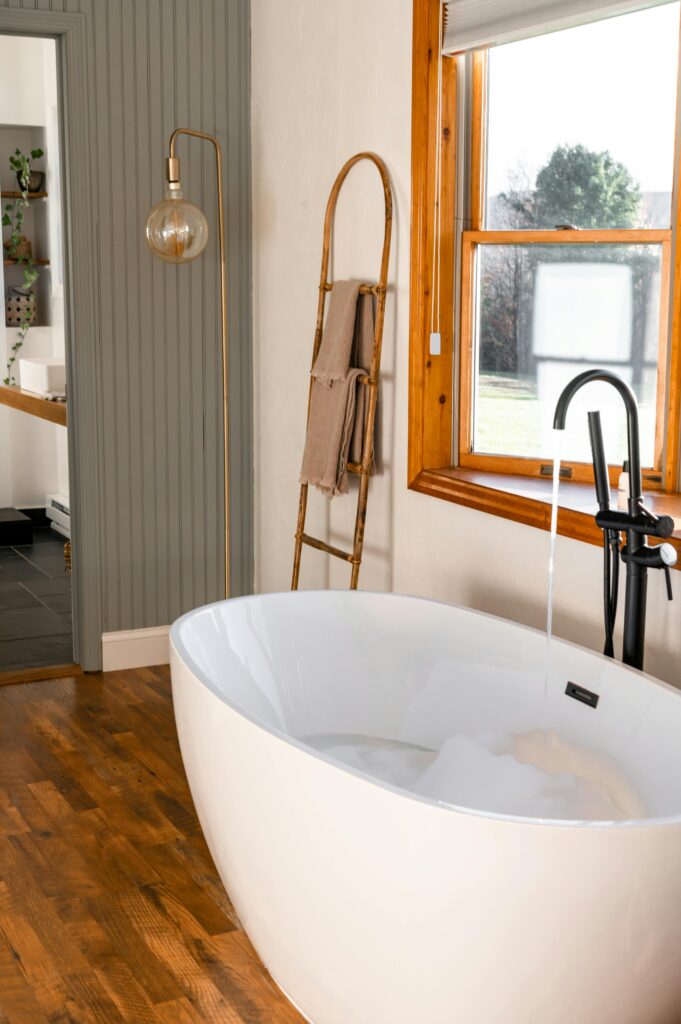 well-lit bathroom with lamp and large white tub with a black faucet