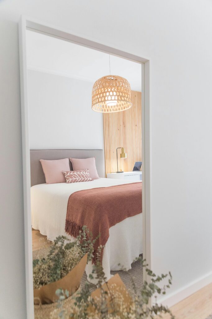 mirror in bedroom with white bedding and wicker light