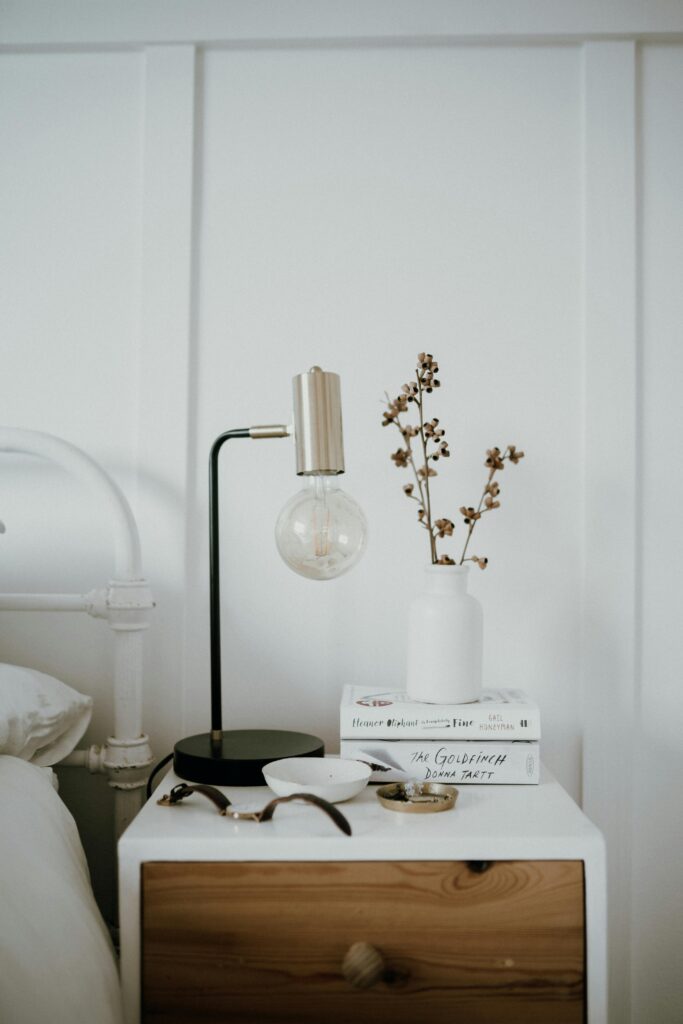 bedroom night stand with lamp and books and a plant with a vase