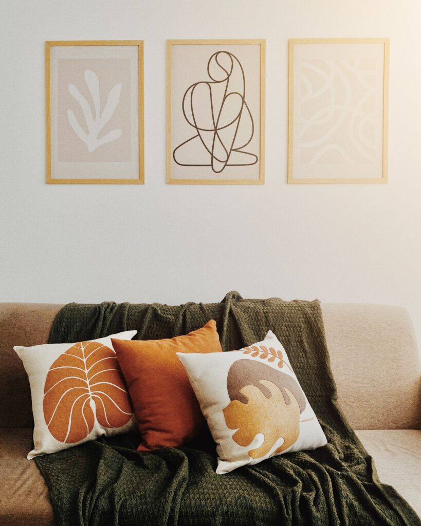 3 fall photos on the wall above a couch that has 3 throw pillows and a green blanket