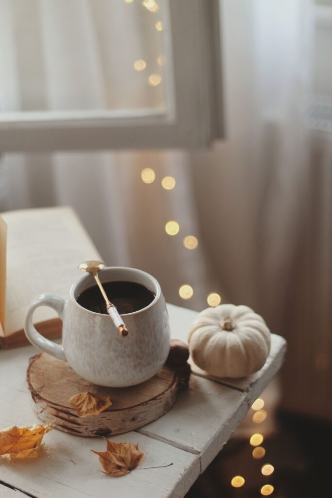 twinkle lights along white curtains with coffee mug and a white pumpkin on a wood table