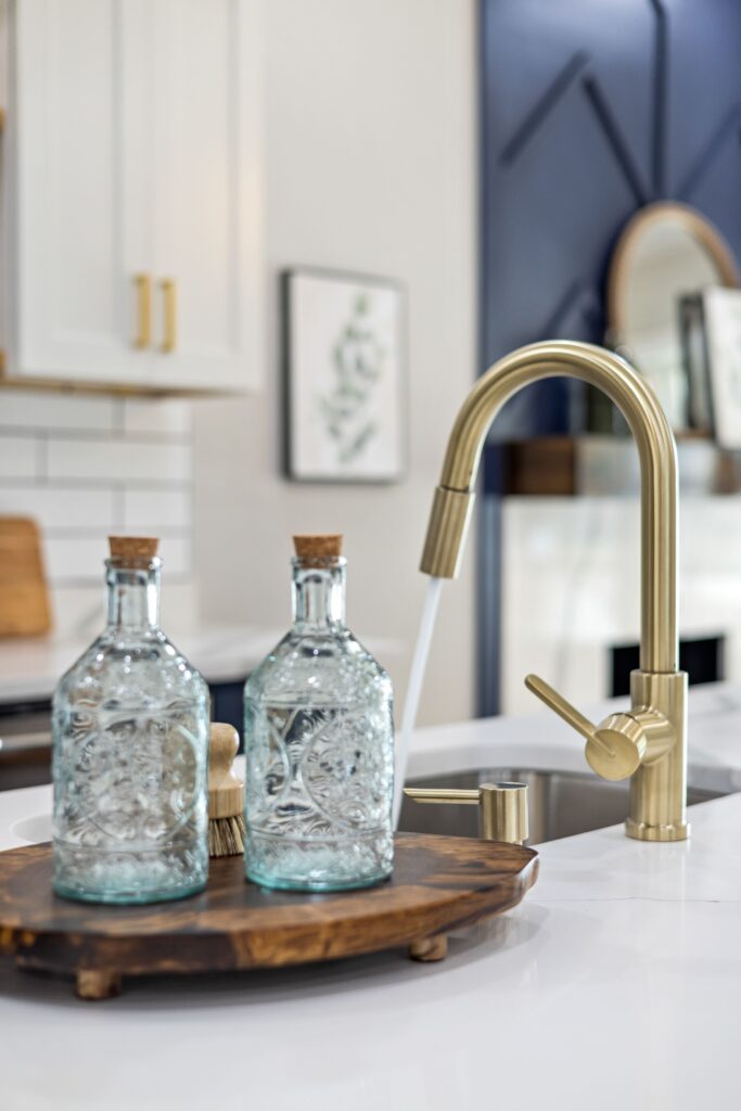 brass kitchen sink with a wooden tray holding glass soap dispensers