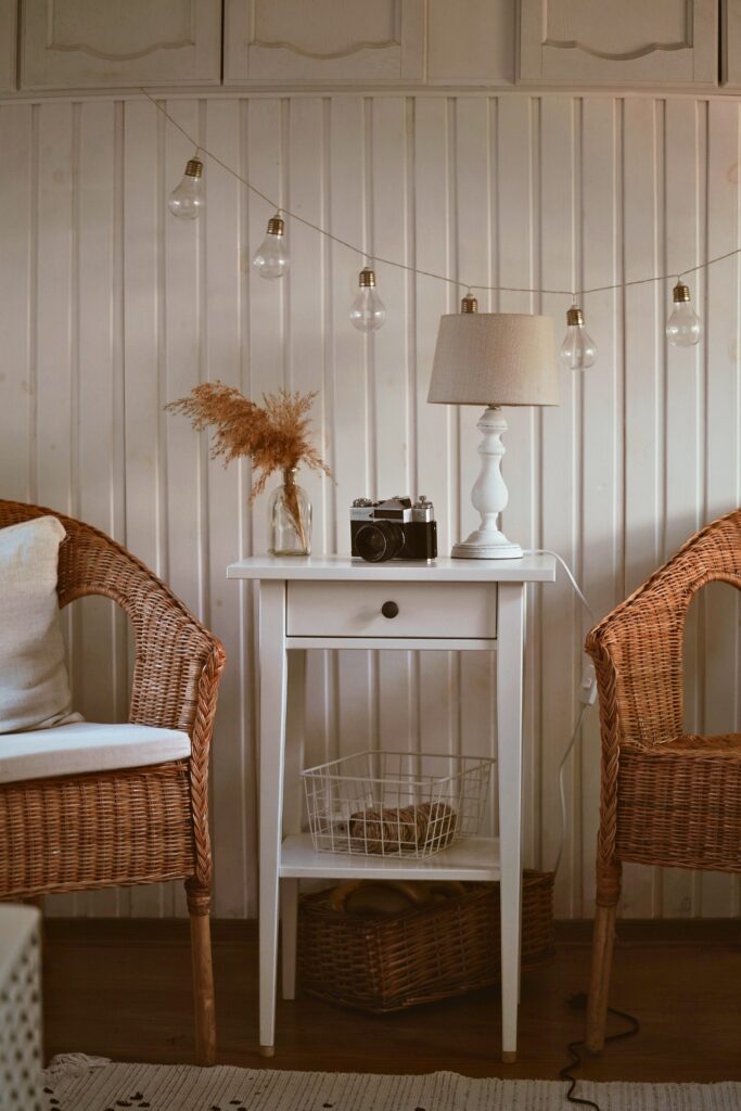 2 wicker chairs with a table in between them and a lamp. Hanging lights on the wall