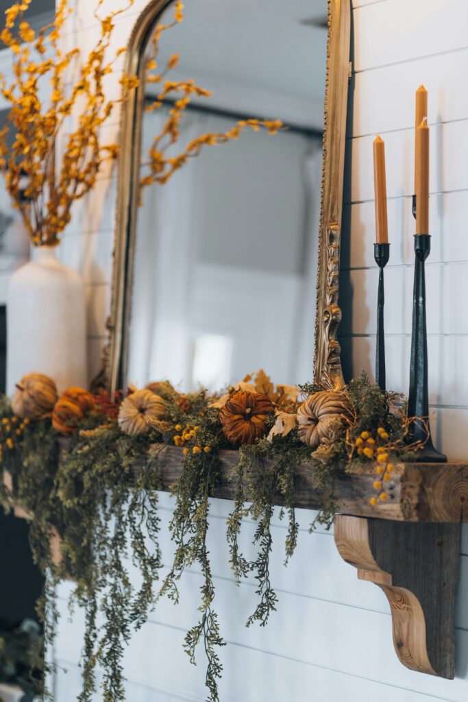 fall decorations for the home with a garland on a mantle and pumpkins along with candles and faux plant