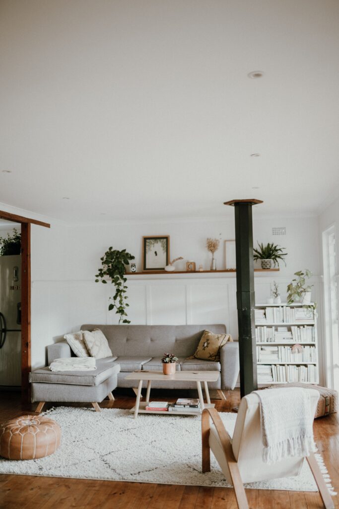 Bright rental living room with a large neutral area rug, gray sectional sofa, wooden coffee table, and indoor greenery.