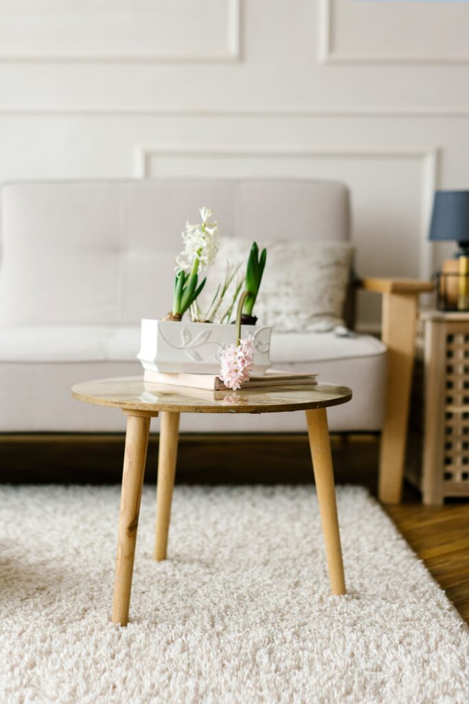 Small wooden coffee table styled with fresh flowers and books in a neutral living room, showing simple rental decorating ideas.