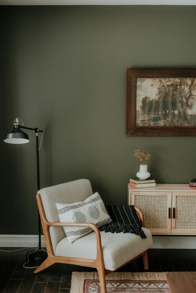 Olive-green living room with neutral furniture, natural wood accents, patterned textiles, and vintage artwork creating a cohesive decorating style.