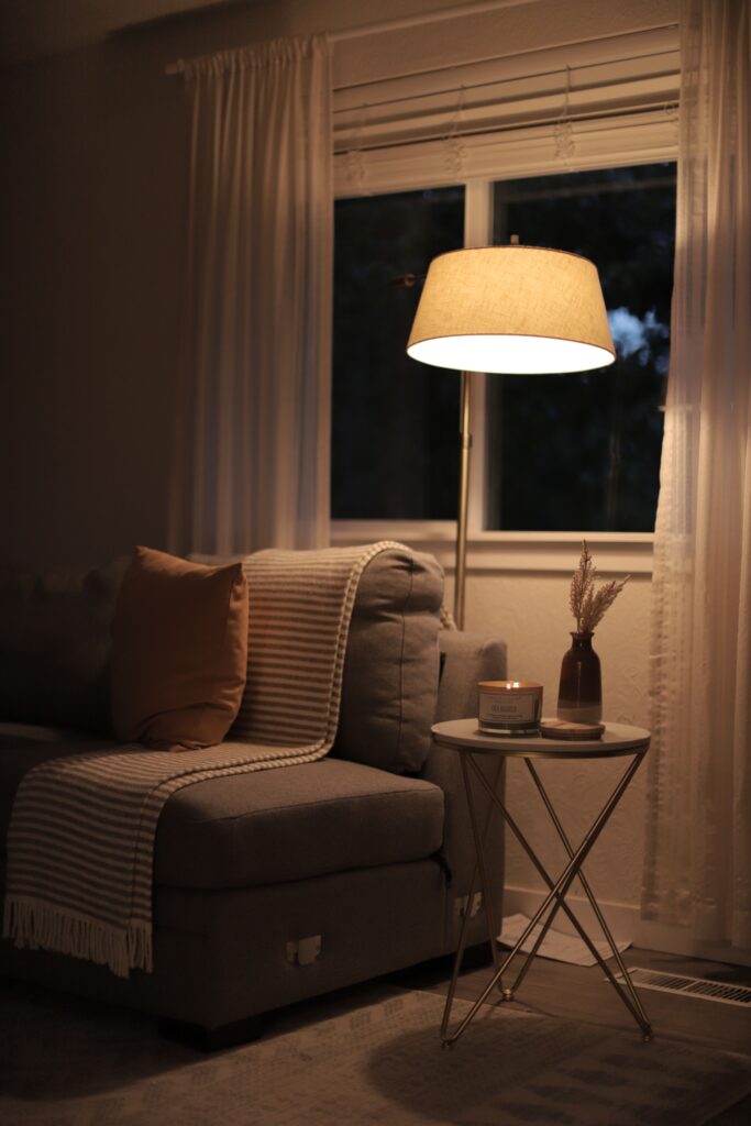 Warm floor lamp illuminating a cozy living room corner with a gray sofa, throw blanket, and decorative pillows.