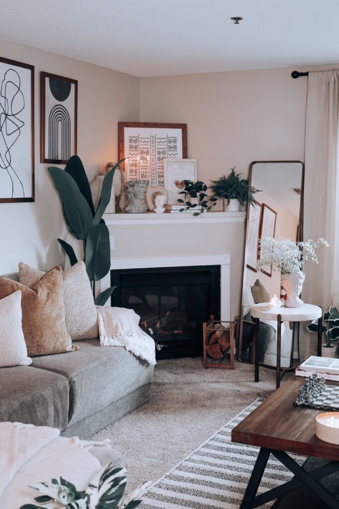 Cozy rental living room featuring framed wall art, a leaning floor mirror, neutral pillows, and a decorated fireplace mantel.