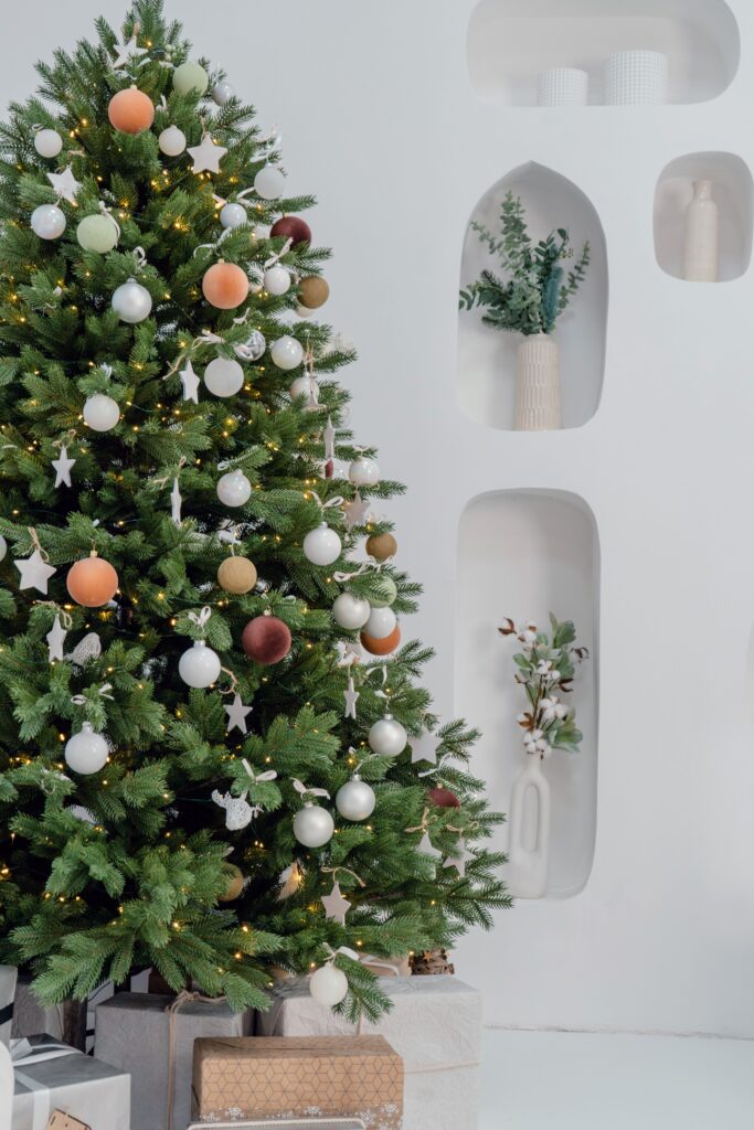 Neutral Christmas tree decoration ideas featuring soft peach, sage green, and white ornaments, wooden stars, and warm white lights.