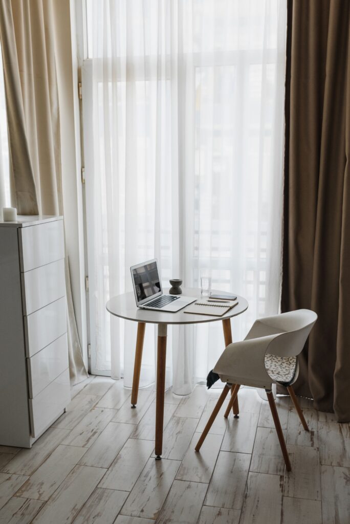 Floor-length sheer curtains framing a bright window beside a small wooden desk and white chair in a cozy rental home.